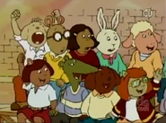 Cheering among the other students. He's the one sitting next to Arthur opposite of Francine.