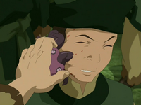 A small, purple, octopus-like creature is pulled from a man's face, leaving behind red markings. The man's face is slightly stretched, and his expression is one of discomfort.