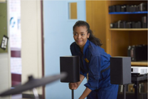 Deviously smiling at Miles, Julie puts down a speaker for her whisper-room practice.