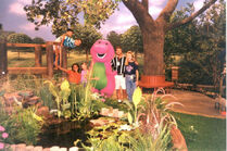 Barney alongside the cast of children from "Once A Pond A Time" with two other individuals.