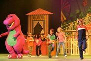 Barney, the kids, and the Balloon Man performing on stage.