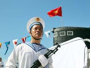 A Vietnam People's Navy sailor poses with his Type 56, behind him is a submarine with the flag of Vietnam.