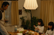 Karin sits at the dinner table while Isshin Kurosaki and Yuzu Kurosaki discuss Ichigo Kurosaki's behavior.