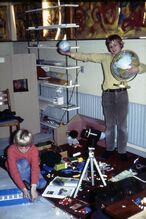 "Lars is playing with Moon and Earth while Henrik is building the air craft carrier. On the shelf you can see the paper sign (rolled) saying "EN REJSE TIL MÅNEN". Behind the camera is the living room where the wives of the astronauts watch the TV transmission of their return."