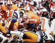 Mark Cotney (No. 33) tackles Wendell Tyler (No. 26), with teammate Bill Kollar (No. 77) watching and Mike Fanning (No. 79)