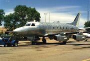 An aged photograph of a small silver jet aeroplane landed on dusty tarmac.