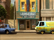 The camera pans out from the Laundromat & Dry Cleaners building with the Mystery Machine parked on the right.