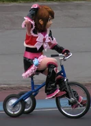A mascot performer of Cure Black on a tricycle.