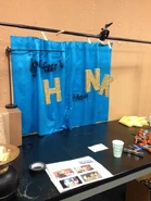 Foto de la carta de título del episodio, hecha con una tela azul con dibujos de notas musicales, letras de cartón de color dorado y brillo, y una bocina, que no aparece en la foto.