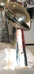 A silver trophy in the shape of an American football—an elliptical shape with pointed ends—standing on a pedestal of the same metal.