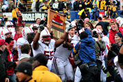 A group of American football players, surrounded by photographers, lift a plaque upon which is an ax head and an inscription.