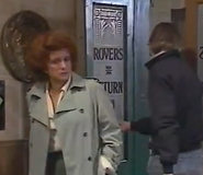 Curly Watts walks out of the Rovers as Elsie walks in.