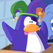 A purple penguin with a green and purple jesters hat pulling a funny face with its tounge sticking out.