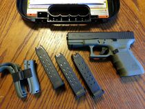 A battlefield green Glock 19 with several magazines and sights.