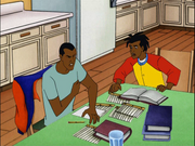 Two black teenage boys are sitting at a table covered in books and papers; one is in pain.