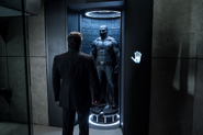 Bruce Wayne standing by the Batsuit