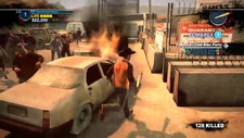 A car burns among zombies and other vehicles.