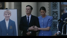 Judge Powell and his wife at a public speaking. They are stood next to a picture of their son.
