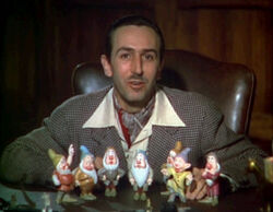 A color photograph of a man sitting behind a desk. Seven figurines are standing before him.