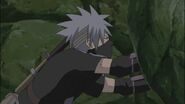 Kakashi trying to push the huge boulder off of Obito.