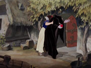 Queen Grimhilde being guided into the cottage by Snow White.