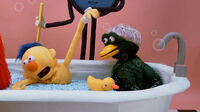 Duck in a bathtub watching as Tony the Talking Clock bathes Yellow Guy.