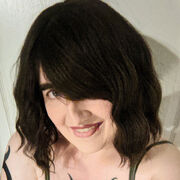 A picture of a smiling woman with brown hair, pale skin, and visible tattoos. She is wearing a tank top with bare shoulders and appears to be looking at the camera.