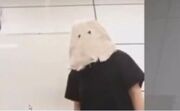 A photo of a woman in a black t-shirt with a sack over her head. The image is a screenshot, with the Windows mouse cursor visible, but it is very low-quality.