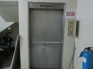 A Mitsubishi floor-type dumbwaiter with hand-operated vertical landing door. Installed in 1990.