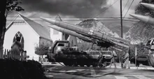 FO4IntroScene6.png (884 KB) Missile carriers on a small-town street