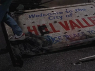 Welcome to the City of HELL VALLEY. In 1985A, the "I" in the greeting sign has been defaced by spray paint, crudely altered, riddled with bullet holes and knocked to the ground