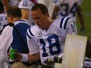 A man holding a green paper cup. He is wearing a white jersey with blue stripes and a blue "18" on the front, which also has a logo with a white "C" above one gold and three white stars. Other men wearing white jerseys with blue numbers and names are visible in the background.