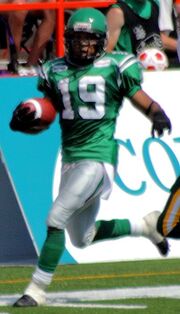 man in green Canadian football uniform runs with a football on a football field