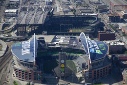 Two stadiums in an industrial area. Both have roofs with large arched trusses.