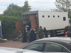 Knights and peasants congregate behind a trailer.