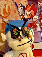 A bootleg Boyfriend plushie with Pico pins over his eyes, seen in front of a detail of the giant FNF poster with Pico and Monster.