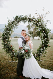 Josie and Kelton on their wedding day, standing in front of a floral arch