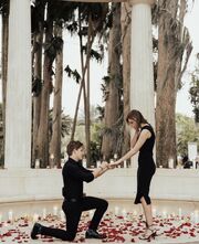 Jackson, on one knee proposing to Emerson, both wearing black outfits
