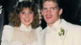 Gil and Kelly, in 80s fashion, smiling at the camera on their wedding day