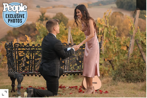 Lawson, down on one knee to Tiffany, who is wearing a pink blush dress. they have the beautiful Tuscan landscape behind.