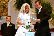 Josh and Anna lighting a candle on their wedding day, with John in the background