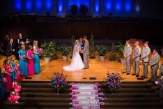 John and Alyssa exchanging vows in the church, their bridal party around them