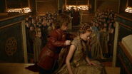 Tyrion tries to wrap his cloak around Sansa, but due to his short height she has to stoop so he can reach.