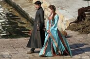A set photo of Ros and Littlefinger. By Season 3, Ros is the head prostitute running the brothel, and her clothing improves to a dress very clearly imitating Cersei's style popular among noblewomen: an asymmetric kimono-like wrap (moreso than in her last dress) and large billowing sleeves.