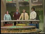 Chuck with the contestants after a round. The scoreboards now have five-figure displays (excluding the "$"). Notice the scoreboard behind the contestant on the right. Currently it shows the accumulated total winnings.