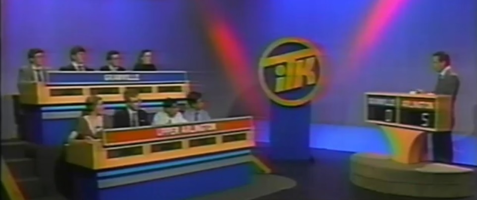 The set for “In the Know” seasons 29 and 30, airing on WOSU from 1993 to 1995, featured a darker blue and pink background with dark brown podiums for the host and student contestants. The ITK logo was added to the podium stand in the middle of the set next to the host and student contestants. The carpet on the student podiums was changed to black. The score numbers were brighter than the team names, which were in blue and red rectangles. A dark blue backdrop was behind Schiffman.