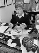 Lt. Col. John F. Pyle shows Eyeglass Inserts for Gas Masks, December 10, 1985. A Scott XM40 and an Avon US10 lie on the table. Optical Inserts for the US10 can be seen on the table at the far left as well.