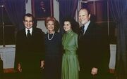 Two women are flanked by two men in suits, standing in a room of the White House.