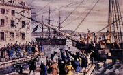 Two ships in a harbour, one in the distance. On board, men stripped to the waist and wearing feathers in their hair are throwing crates overboard. A large crowd, mostly men, is standing on the dock, waving hats and cheering. A few people wave their hats from windows in a nearby building. Monopolistic activity by the company triggered the Boston Tea Party.