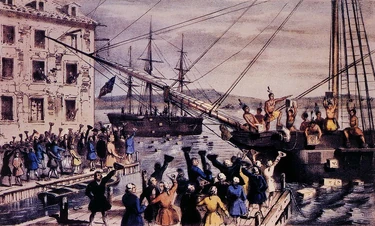 Two ships in a harbor, one in the distance. On board, men stripped to the waist and wearing feathers in their hair throw crates of tea overboard. A large crowd, mostly men, stands on the dock, waving hats and cheering. A few people wave their hats from windows in a nearby building.